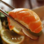 Mouthwatering salmon nigiri sushi held by chopsticks, ready to eat.